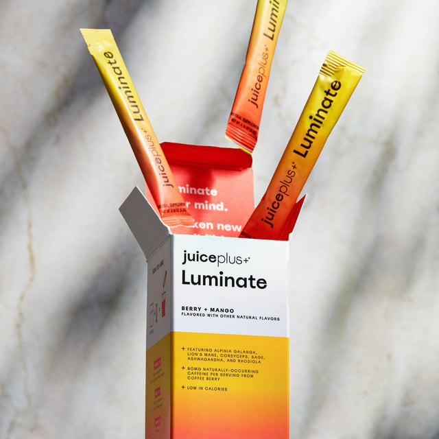 Juice Plus+ Luminate supplement sachets coming out of the box on a marble surface