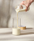 Person pouring Juice Plus+ Complete from a glass container into a glass on a neutral background