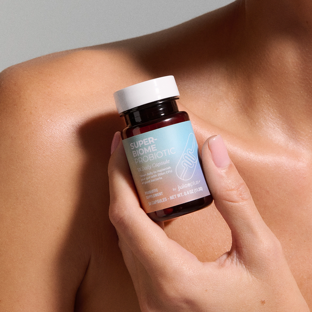 Hand holding a bottle of Juice Plus+ Super Biome Probiotic against a neutral background