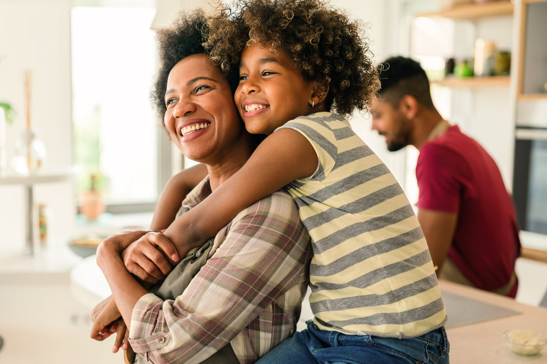Woman hugging a child in a kitchen with another person in the background