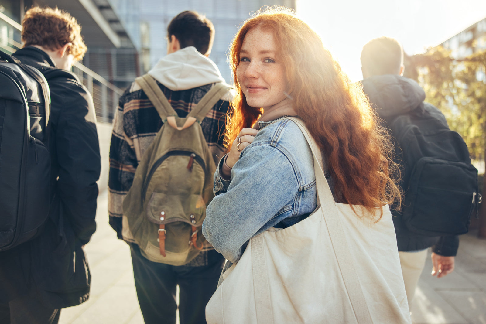 Woman with red hair holding a white bag, surrounded by people with backpacks in an urban setting.