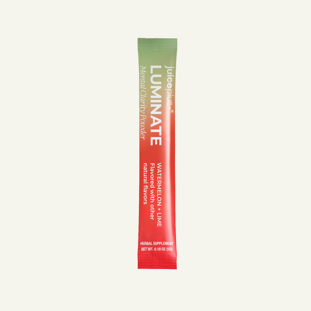 A single-serve stick pack of Juice Plus + LUMINATE herbal supplement, Watermelon + Lime flavor, featuring a vertical gradient from green to red-orange with white text, centered on a light cream background.